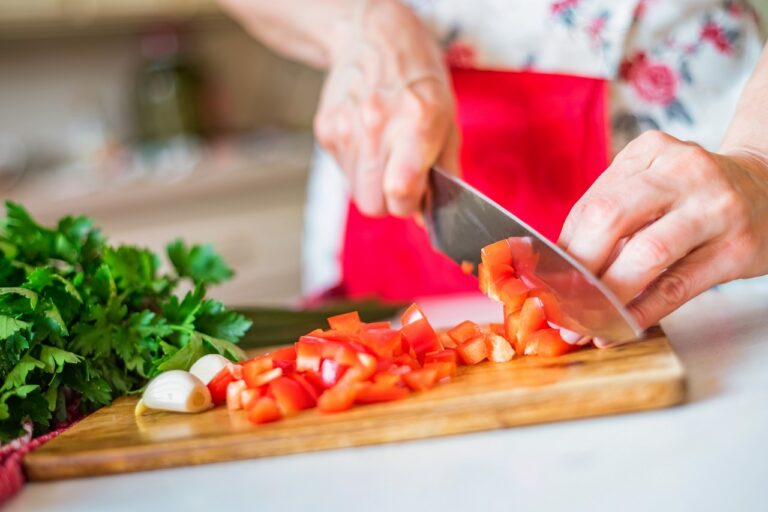 Female hand with knife cuts bell pepper in kitchen. Cooking vegetables